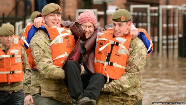 Soldiers carry a woman through flood waters