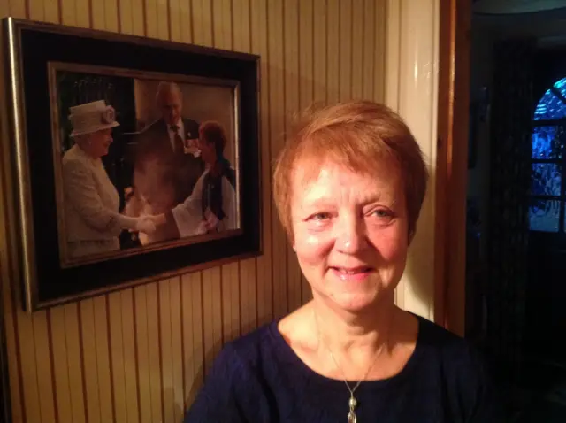 Pauline Simpson, at home, with a photo of the Queen in the background