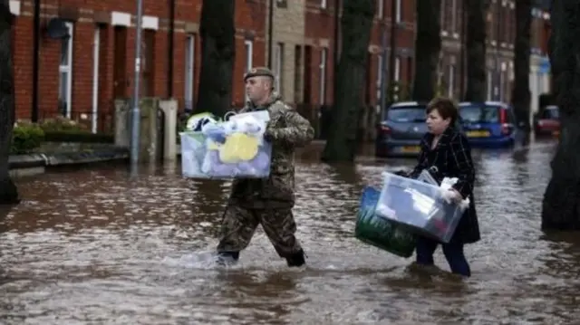 People carrying belongings through floodwater