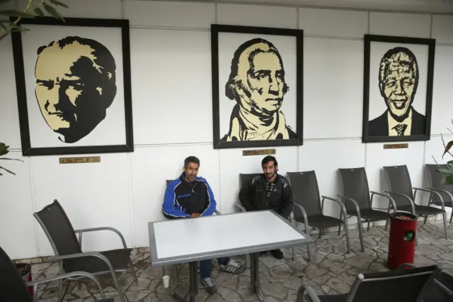 Palestinian (L) and a Syrian asylum applicant sit under portraits of past presidents, including Kemal Ataturk of Turkey (L), George Washington of the United States (C) and Nelson Mandela of South Africa, at the former Hotel President where the two men now live on December 9, 2015 in Berlin, Germany