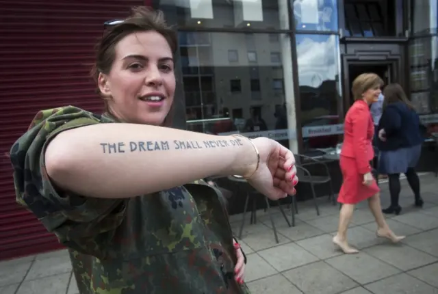 A member of the public shows a tattoo that reads "The dream shall never die" as First Minister Nicola Sturgeon is on the campaign trail in Paisley