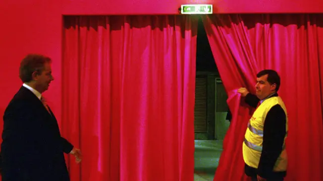 Tony Blair being led through a curtain beneath a sign reading "exit".