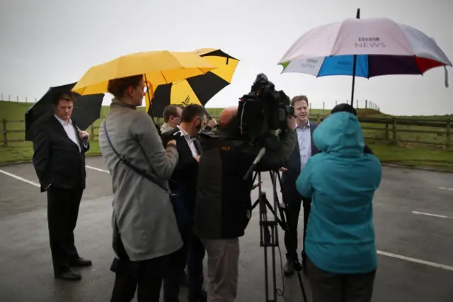 Liberal Democrat Danny Alexander (left) stands under an umbrella as party leader Nick Clegg (second from right) gives a television interview