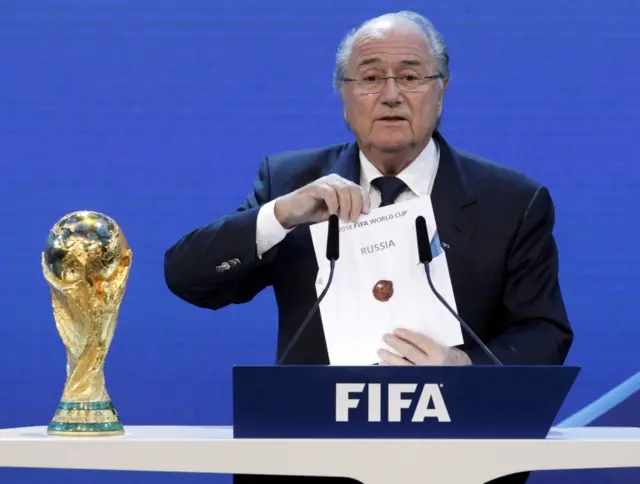 Sepp Blatter pulling a card saying "Russia" out of an envelope