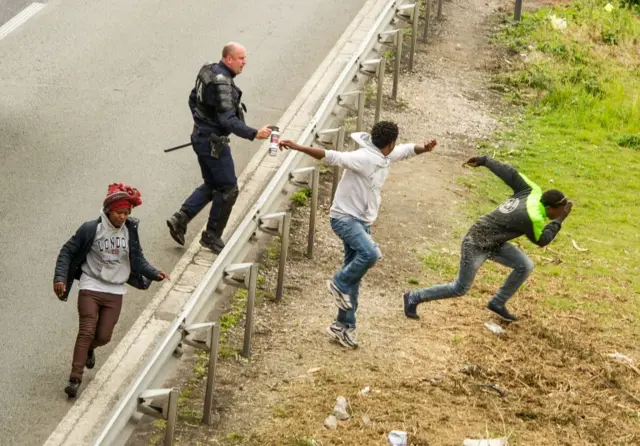 French policeman sprays tear gas at migrants trying to enter the Channel Tunnel