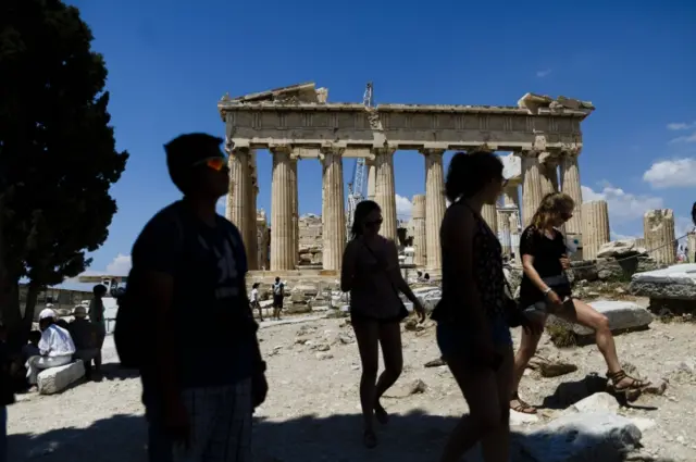 Tourists walk trough the ancient Acropolis hill, with the ruins of the fifth century BC Parthenon temple on the background in Athens