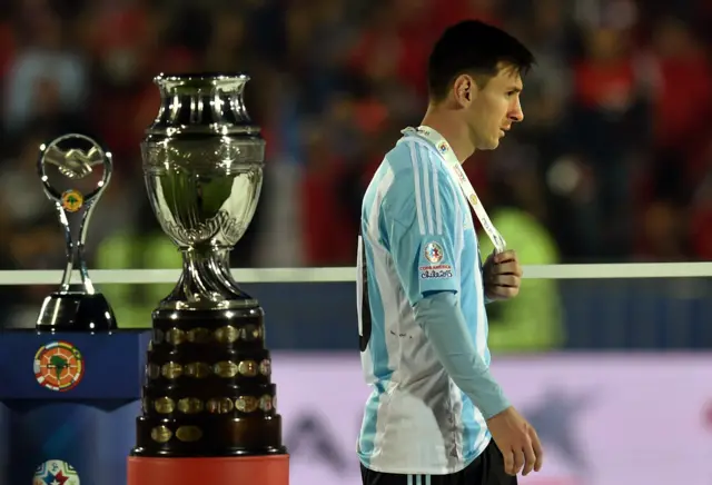 Lionel Messi walks past the trophu