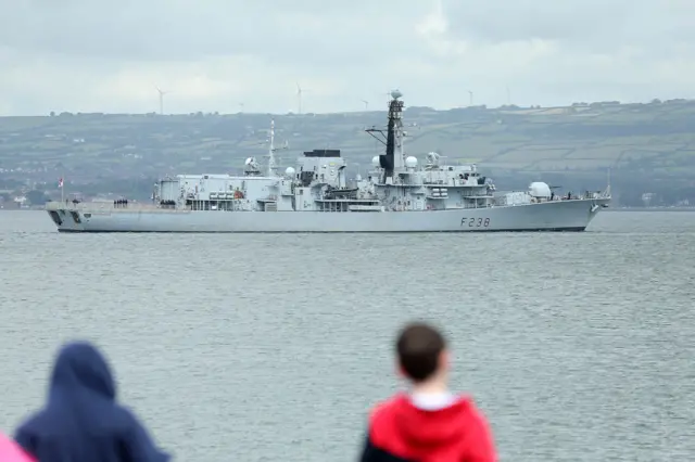 Crowds watch a naval vessel leave Belfast Harbour