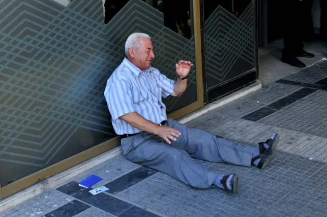 A distressed pensioner sits on the ground outside a national bank branch, as banks opened only for pensioners to allow them to withdraw their pensions, with a limit of 120 euros, in Thessaloniki, on July 3, 2015.