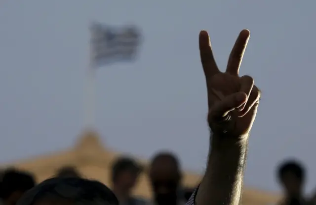 A "No" supporter flashes a victory sign before a Greek flag atop the parliament in Athens, Greece 5 July, 2015