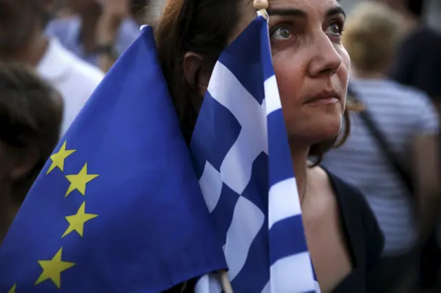 A pro-Euro protester holds a European Union and a Greek national flag during a rally in front of the parliament building in Athens, Greece, July 9, 2015.