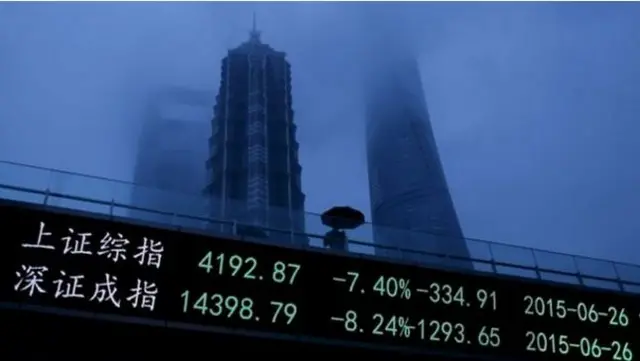 Chinese person holds umbrella whilst walking past boards showing stock price falls