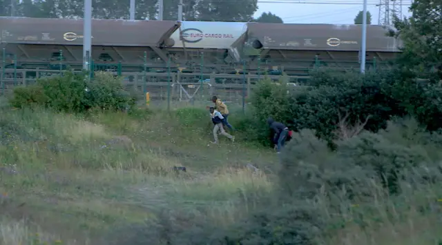 Migrants run near a fence leading to the Eurostar railway tracks after being spotted by police