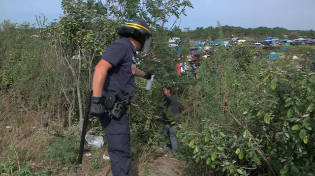 A French police officer threatens a migrant with pepper spray to stop him approaching lorries on a motorway