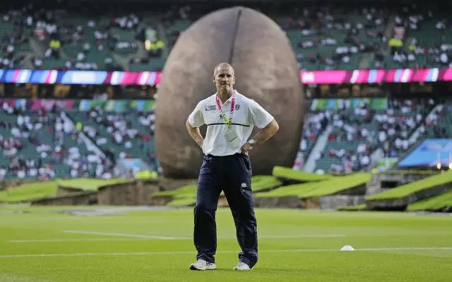 Stuart Lancaster stands in front a large rugby ball