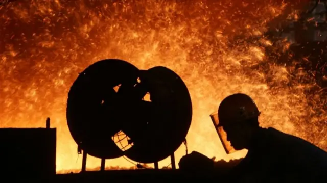 A steel worker labours in front of a blast furnac