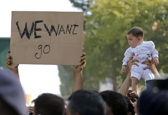 A man lifts a child as migrants protest at the railway station in Tovarnik, Croatia