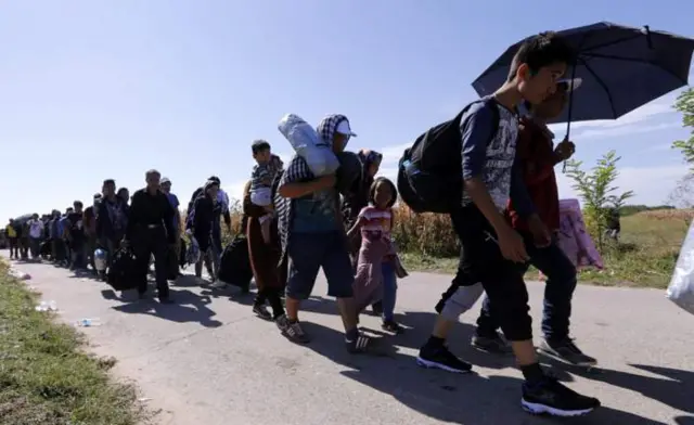 Refugees shelter from the sun as they walk near the Croatian-Serbian border