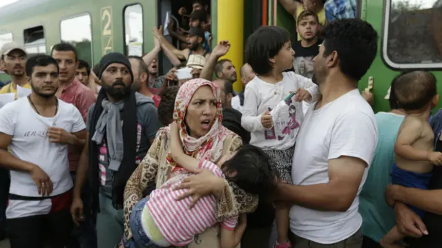 A woman carrying a child stands outside a train carrying migrants that was stopped in Bicske, Hungary - 3 September 2015