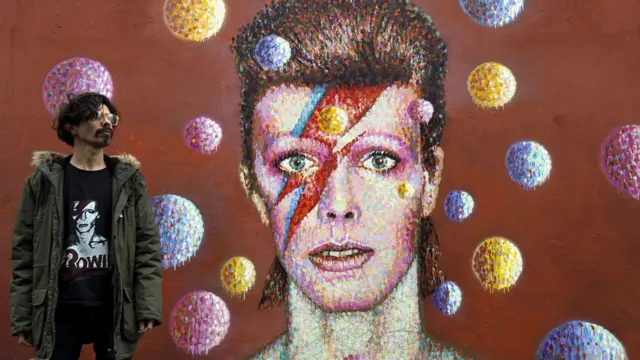 A fan stands next to a mural of David Bowie in Brixton, south London