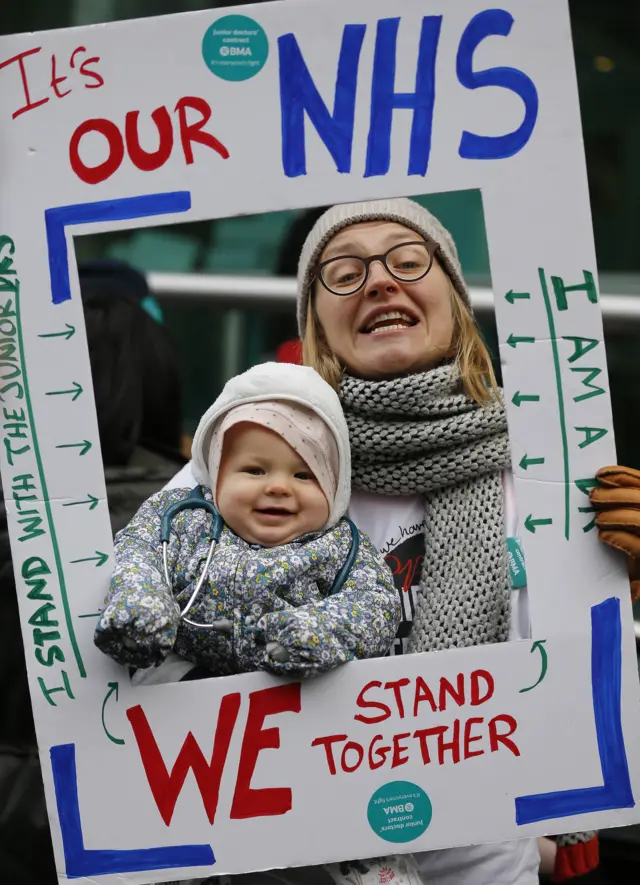 A woman poses with her baby in the frame of a protest banner at a strike in London