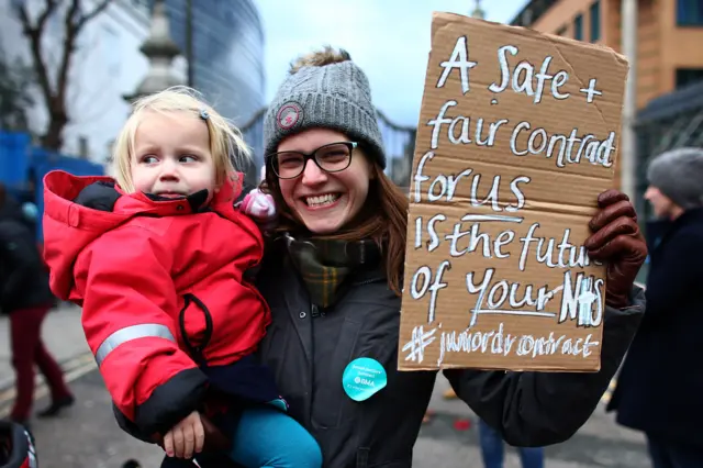 A junior doctor holds her baby and a placard as she takes part in a picket outside London's King's College Hospital on 12 January 2016