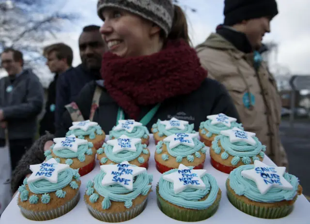 A demonstrator holds a tray of decorated cakes at a strike