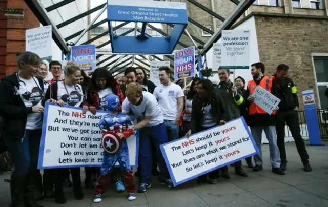 Young patient Frankie Clements in a comic book costume poses with the National Health Service Singers outside Great Ormond Street Hospital for Sick Children