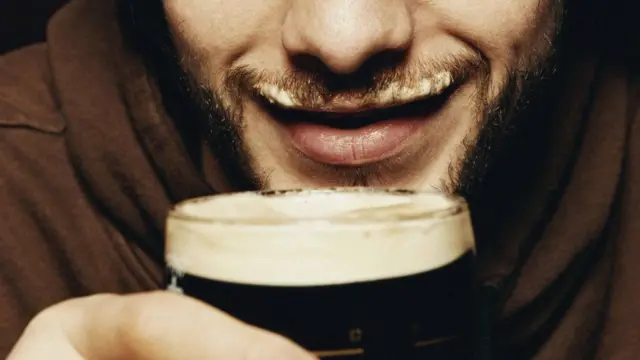 A bearded man drinking a dark beer.