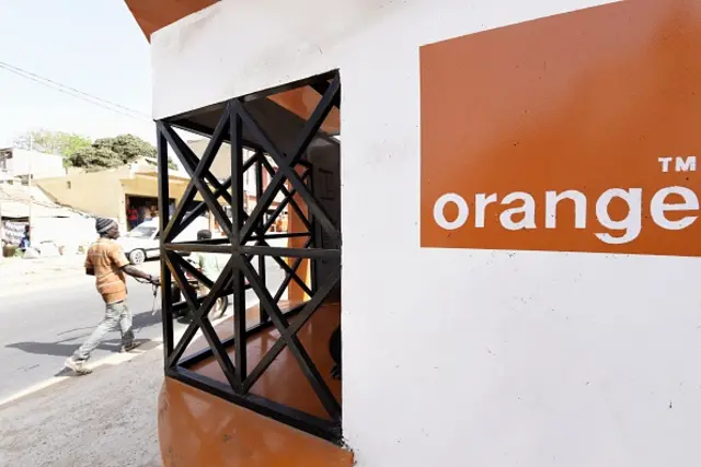 Customers pass in front of an 'Orange Money' booth, on July 7, 2015 in Ouakam, a suburb of Dakar