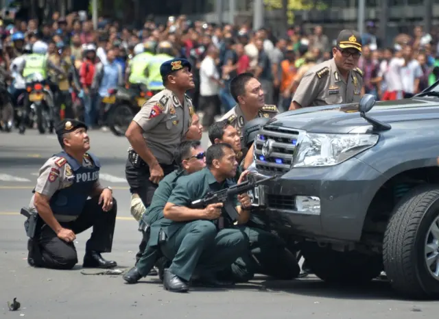 Crowds watch as police take their position behind a car