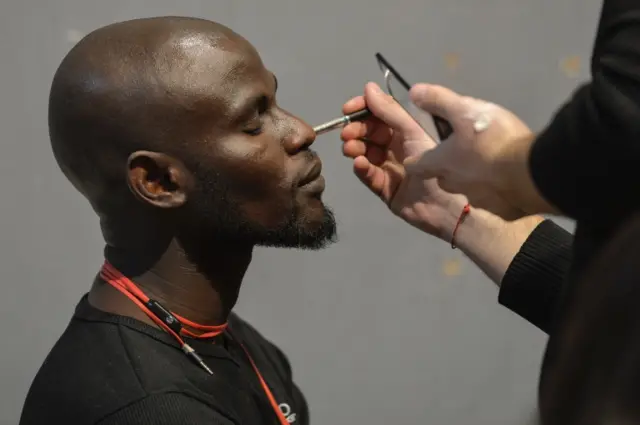 An asylum seeker gets his make-up done backstage prior to taking part in the special event "Generation Africa" during the ITC Ethical Fashion Initiative as part of the Pitti Immagine Uomo 89 in Florence, on January 14, 2016. Asylum seekers from Mali and Gambia model at Florence"s prestigious Pitti Immagine event on January 14, 2016, kicking off an initiative to school would-be migrant fashionistas in Italy