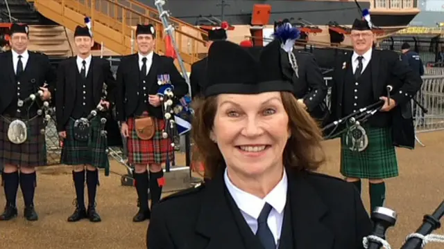 Irene Robinson standing in front of a group of pipers