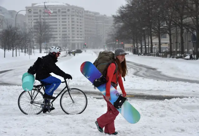 A woman carries a snowboard across DC.