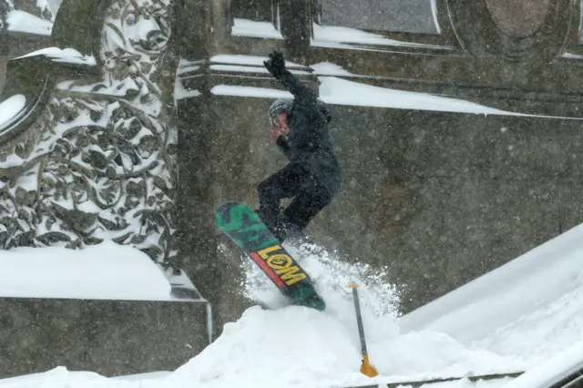 A man jumps on a snow board as snow falls in New York.