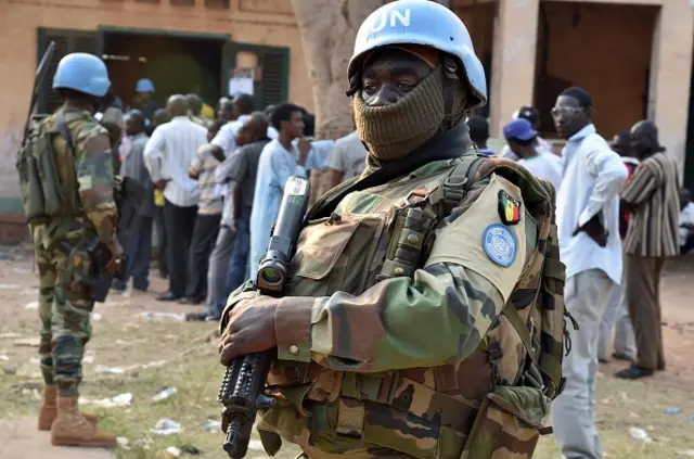 Senegalese UN peacekeeping forces stand guard as people wait to vote at a polling station during presidential and legislatives elections in the streets of the Muslim PK-5 district of Bangui on December 30, 2015