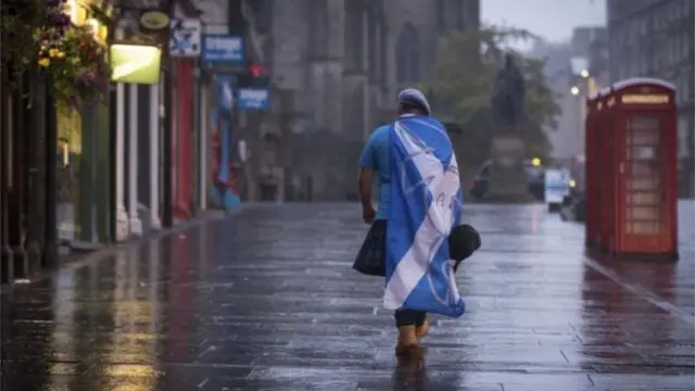 Man with saltire on his back walking away from camera