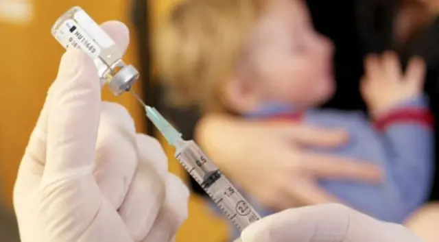 Nurse holding needle and child awaiting jab