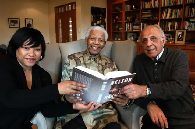 Nelson Mandela poses with a copy of the British edition of his newly released alongside his daughter Zindzi and Ahmed Kathrada