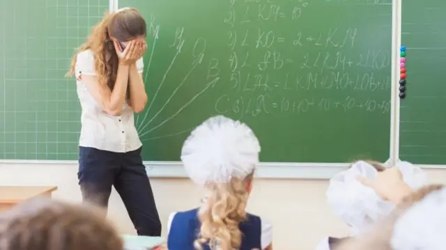 Teacher holds her head in her hands