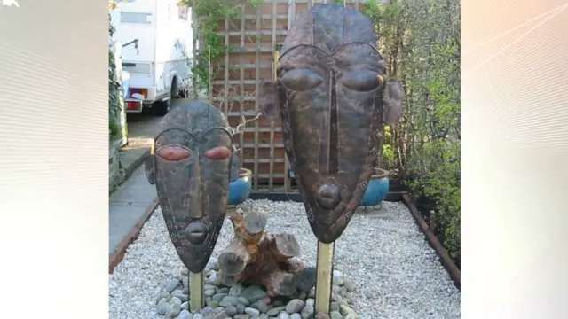 Two tribal mask statues in a pebble garden