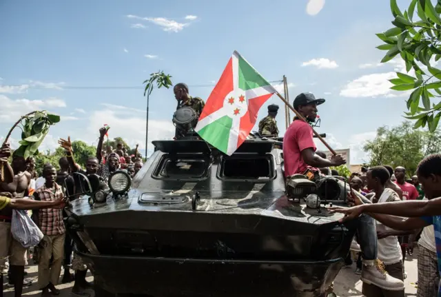 A man holding a Burundi's flag stands on a tank as people take to the streets to celebrate, waving branches, beeping car horns and parading through Bujumbura on May 13, 2015