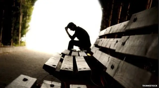 Man sitting on a park bench with his head in his hand