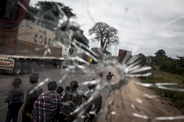 Street vendors are seen through a bus windscren bullet hole alongside the Mozambican Main North South road (NH1) on May 27, 2016 at Nhamapaza in the Gorongosa area, Mozambique.