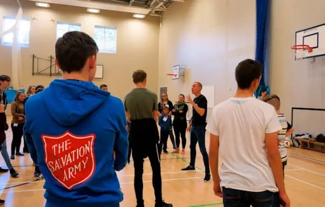 A group of young children, facing a tutor, in a sports hall; One is wearing a Salvation Army sweattop