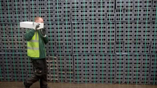 a man carries a breeze block in a builders' yard