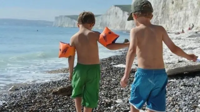 Two children in swimsuits walking on a pebbly beach