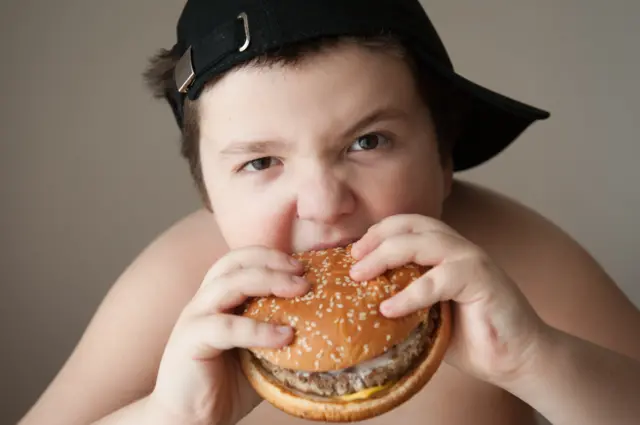 An overweight child eating a burger.