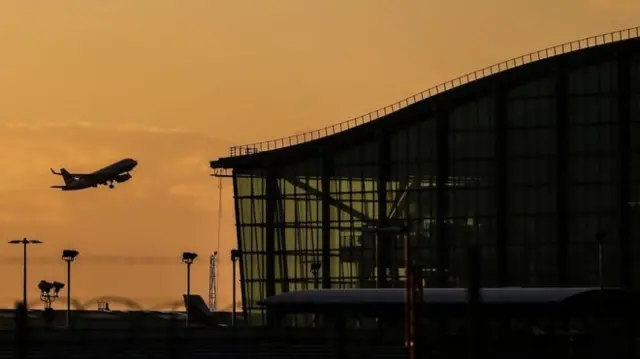 Heathrow Terminal 5 at sunrise with plane taking off