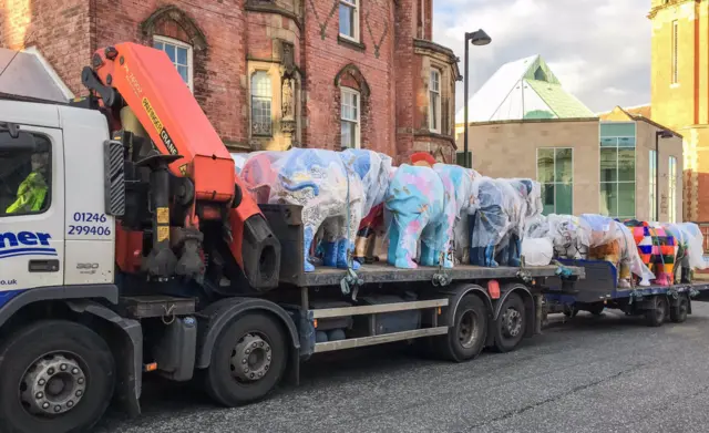 Elephant sculptures being transported on a lorry.